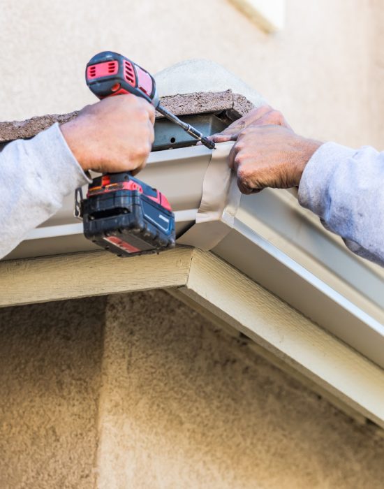 Workers Attaching Aluminum Rain Gutter to Fascia of House Workers Attaching Aluminum Rain Gutter to Fascia of House